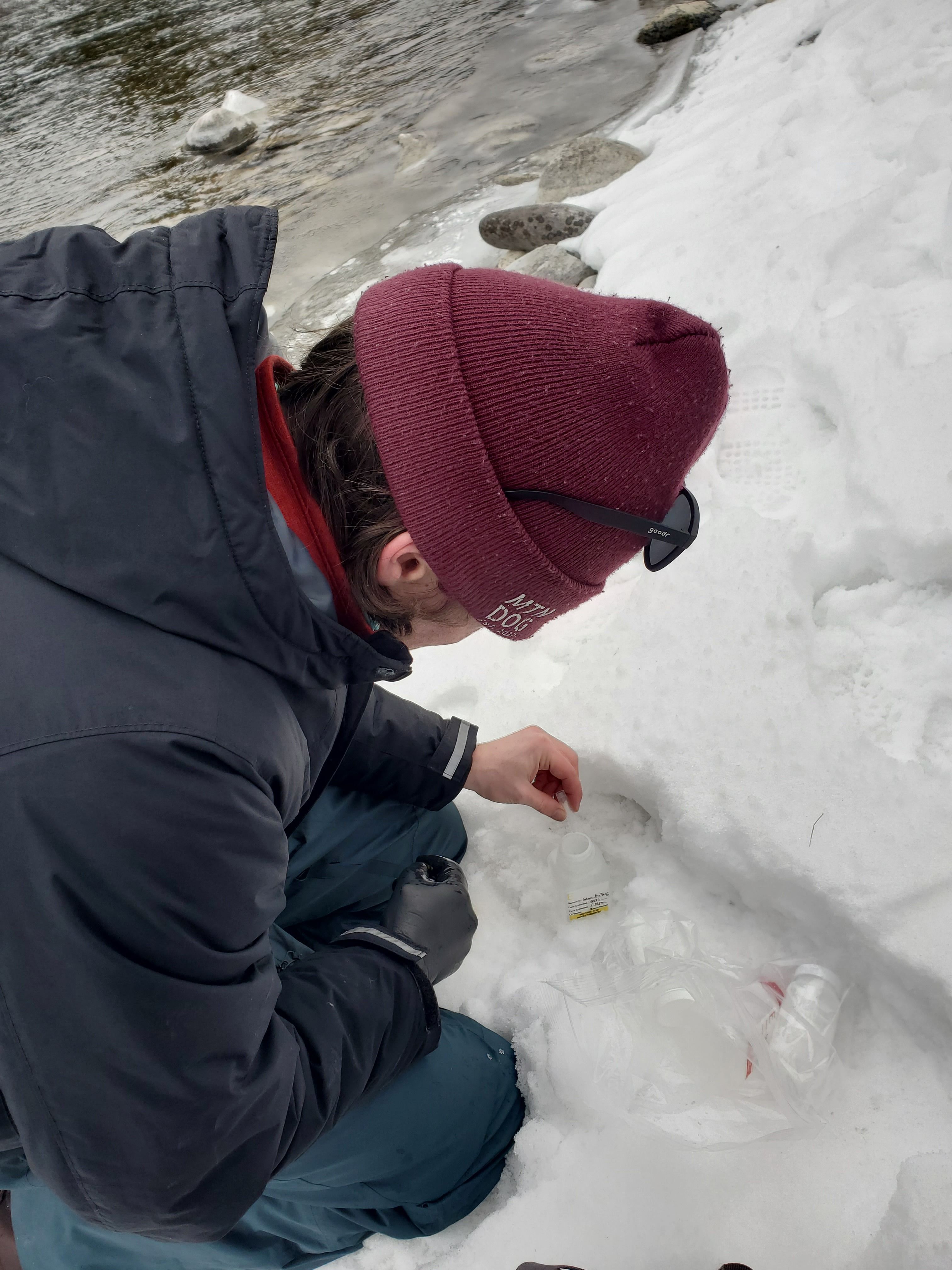 An AmeriCorps member wearing a burgundy beanie drips water into a small container to complete groundwater testing.