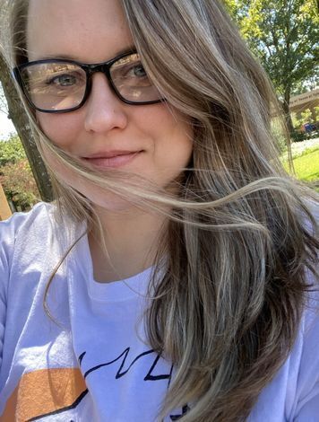 Photo of a white woman with long wavy brown hair and glasses.