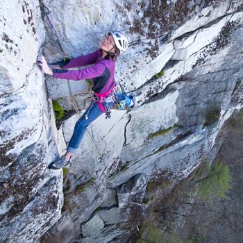 Lynn McGrew balances with a wide stance on the cliff while looking up