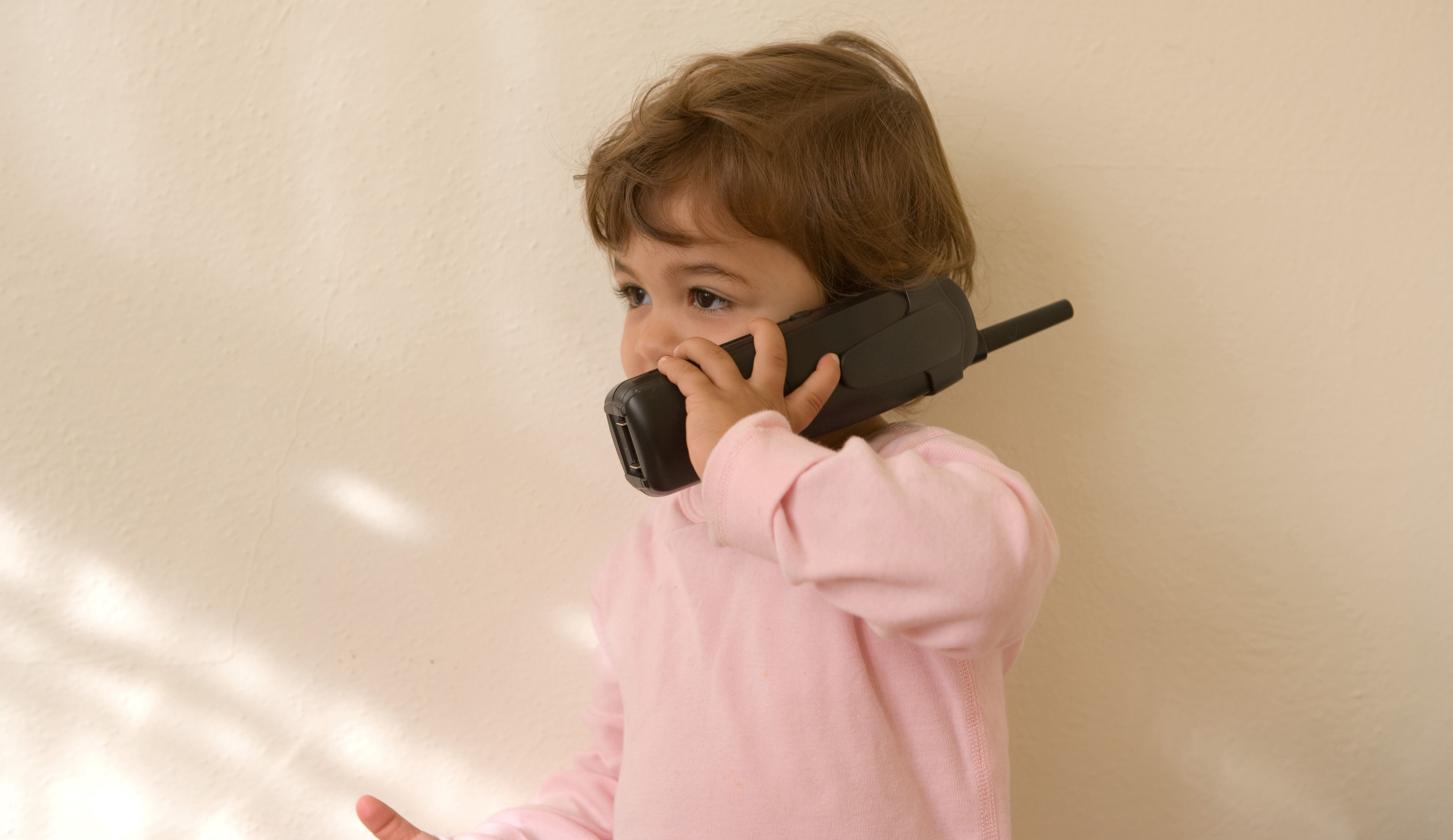 Image of a young girl indoors holding a phone up to her ear. 