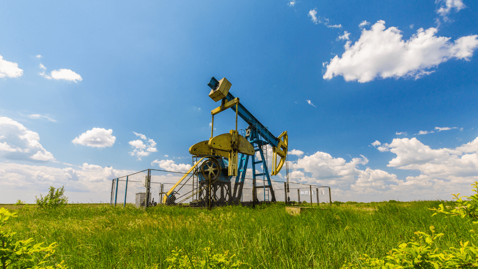 An oil drill on green grass with a blue sky 
