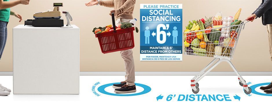 People standing in a checkout line. Near floor and wall graphics promoting social distancing.