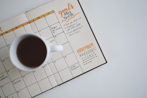 A mug of coffee sitting atop a monthly planner on a table.