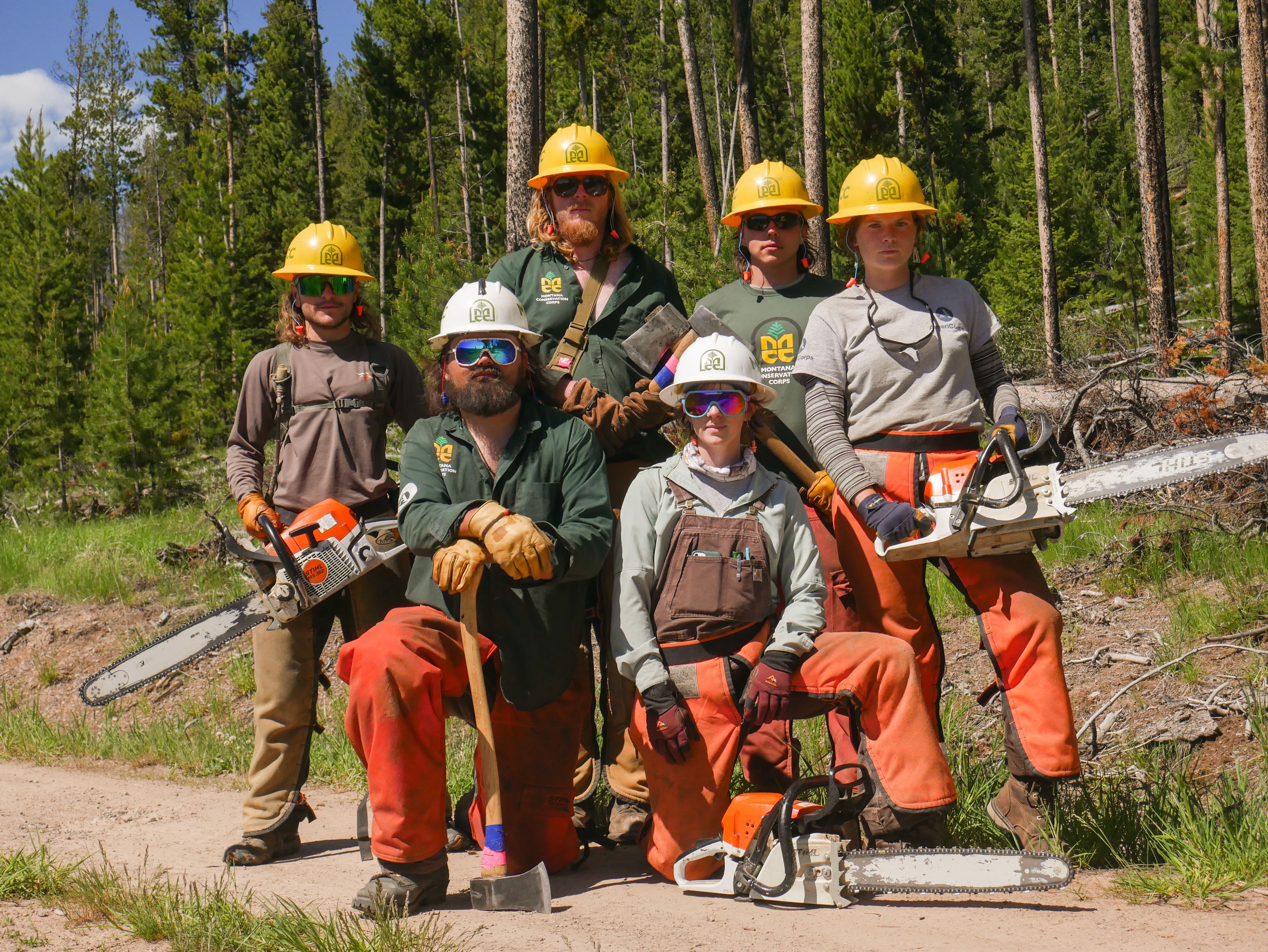 A crew wearing chaps and chainsaws, stands posing with serious faces.