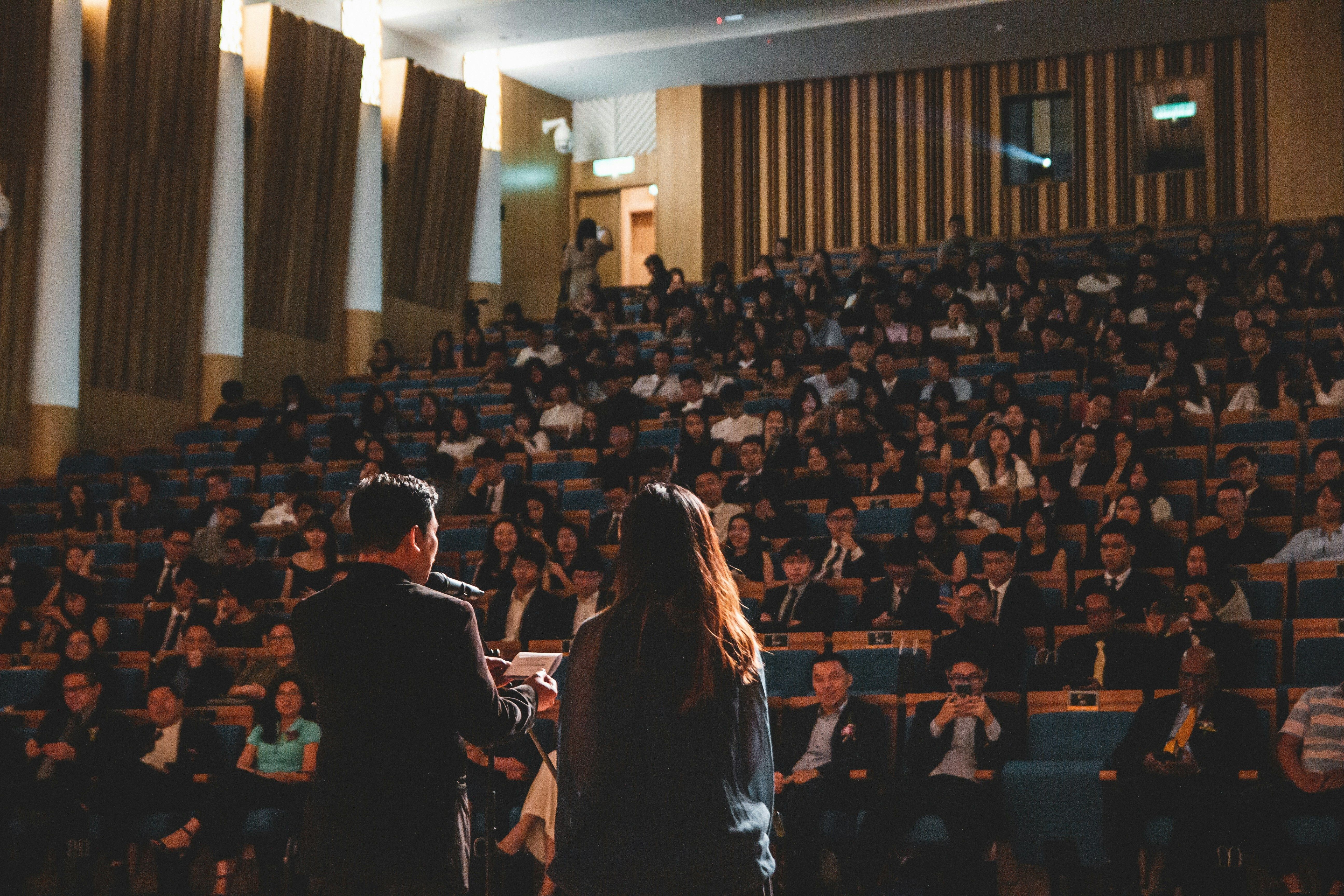 Photo of a speaker in an auditorium speaking to a large crowd. 