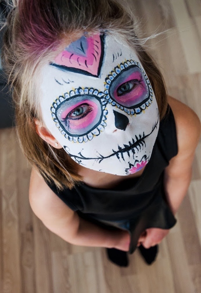 A child wearing colourful Day of the Dead skull face paint.