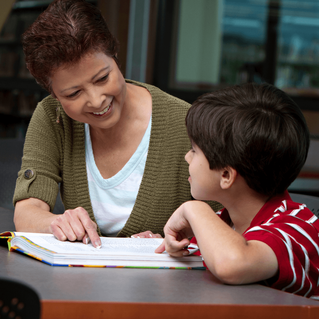 A middle aged woman looking a young boy as they sit next to each other and read.