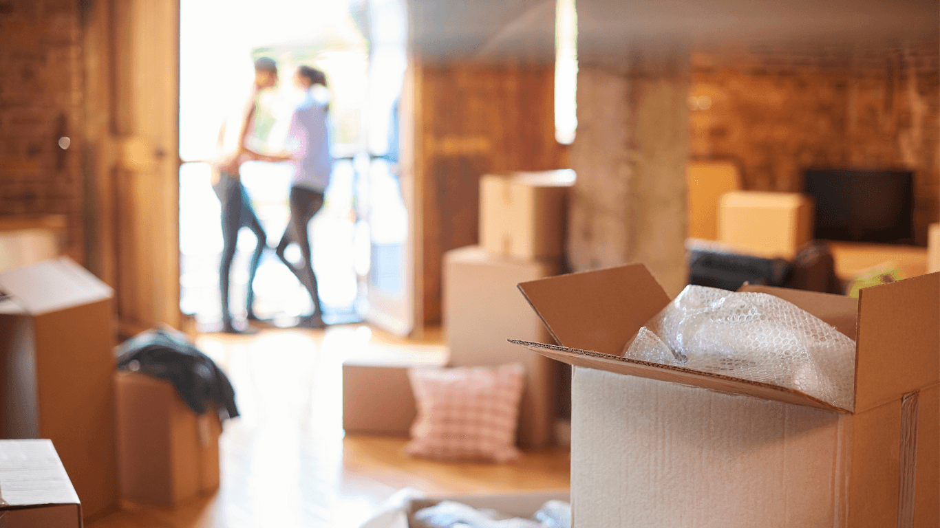 A couple stands on a balcony behind a room full of moving boxes