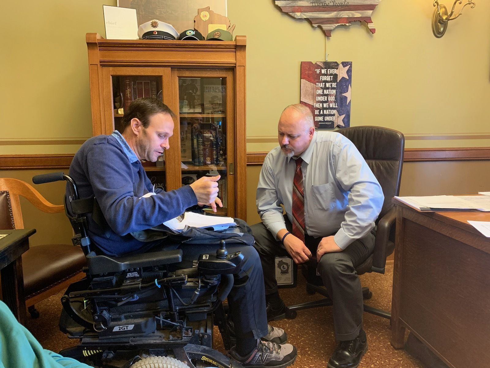 Man in wheelchair (left) talks to man sitting (right)