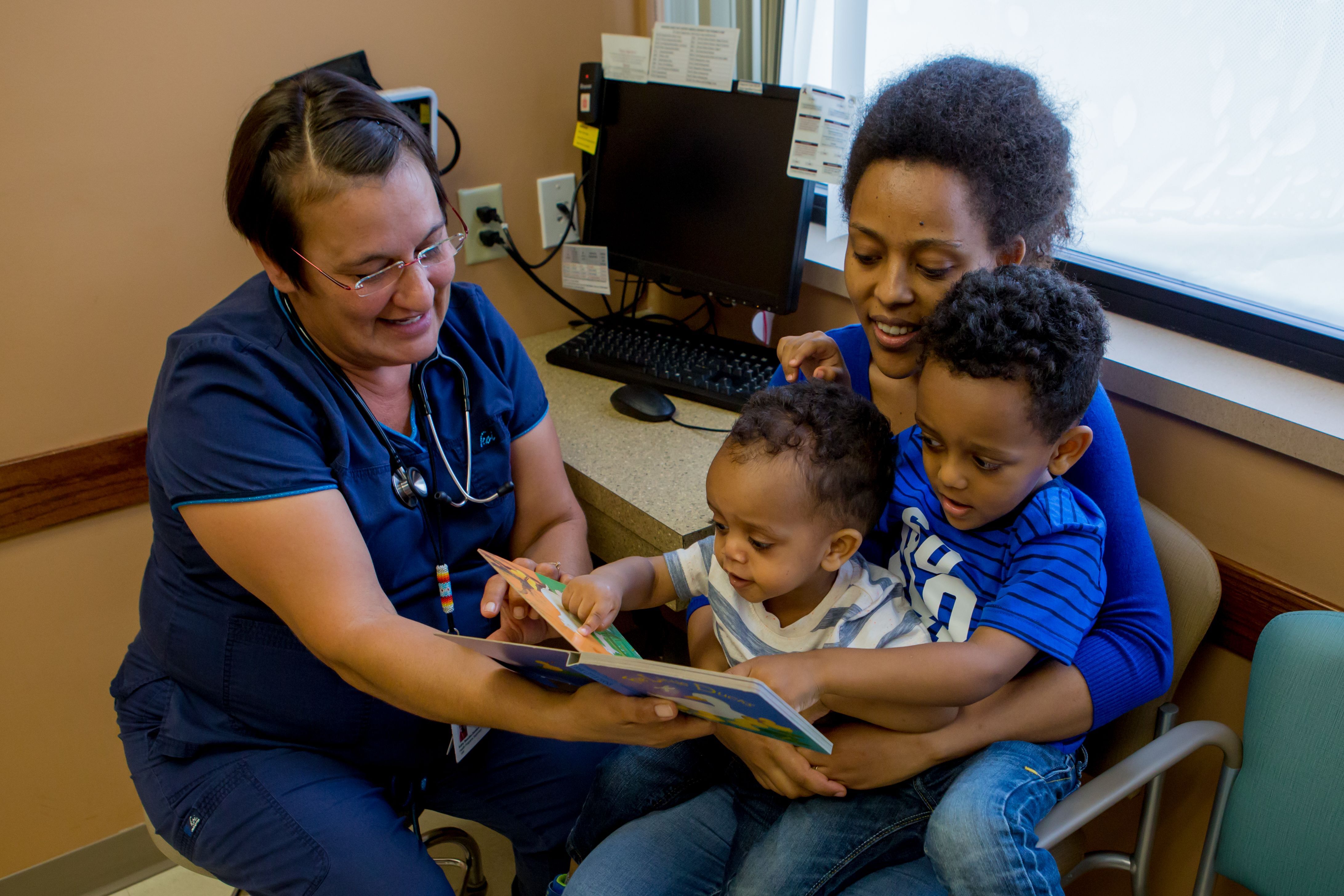 A healthcare provider helping a parent read a picture book to two toddlers.