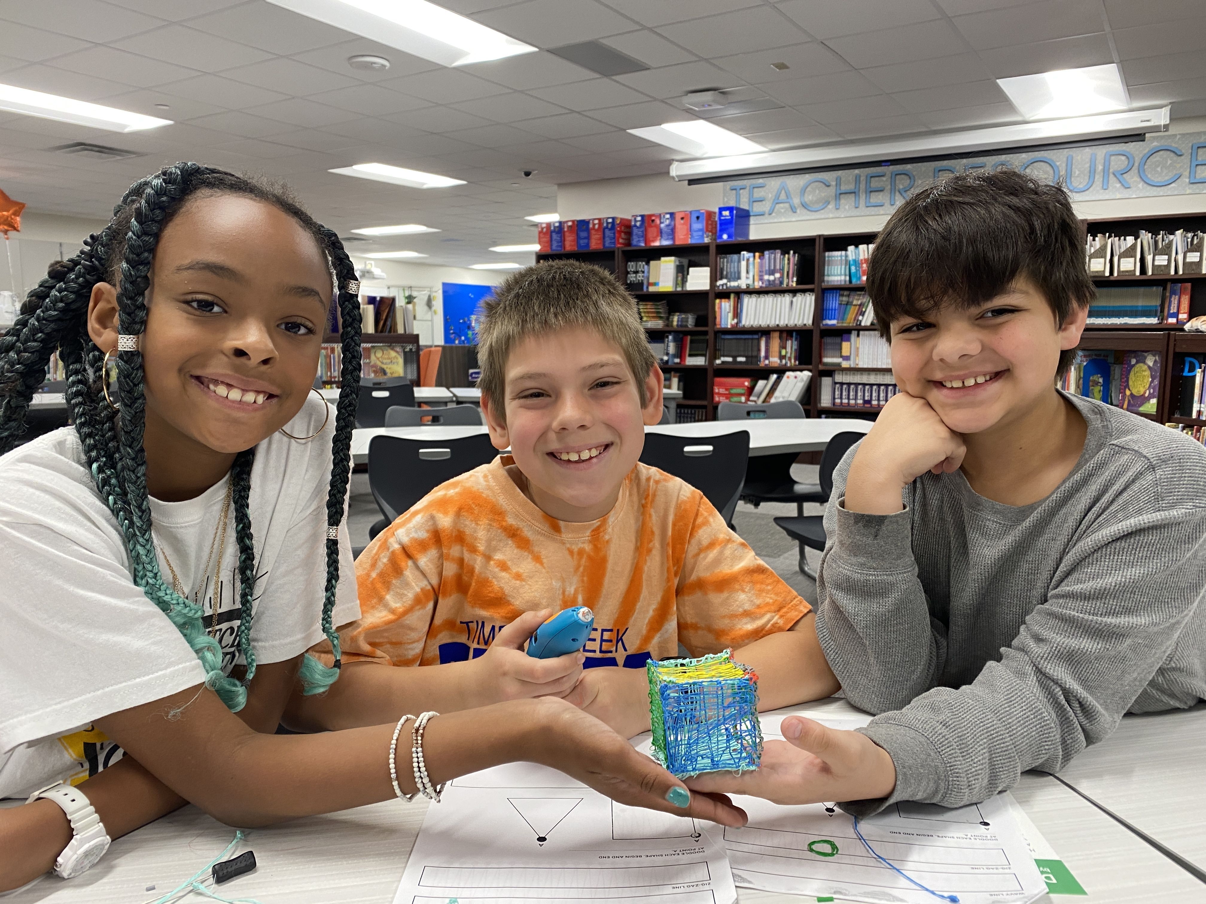 Three students smiling and holding the cube they drew using a 3D pen in Timber Creek's Library Lab.