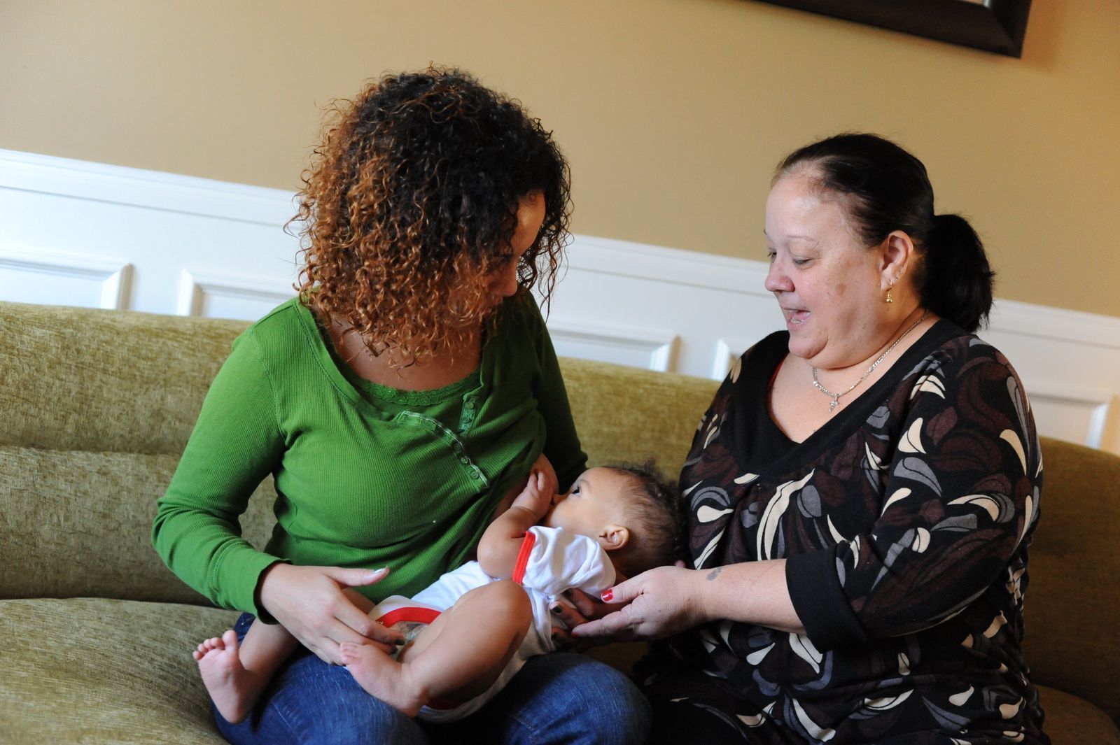 A mother is breastfeeding her infant with the assistance of her mother.