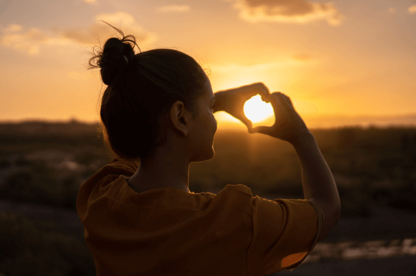 person making a heart out of hands in front of sunset