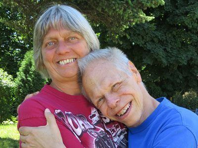 A woman and a man are facing the camera and smiling while hugging