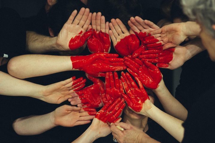 Multiple people's hands coming together to create a painted red heart.