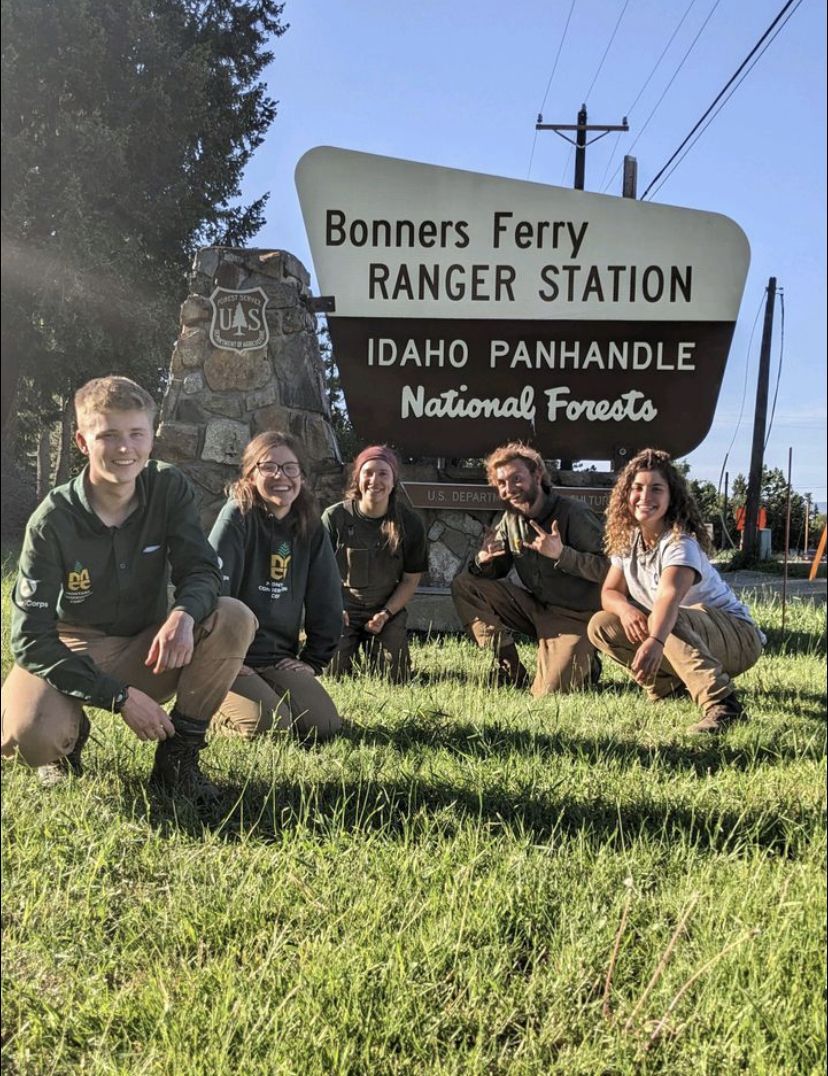 A crew smiles next to a Bonners Ferry Ranger District sign
