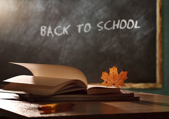 Back to school written on a chalkboard with an open book on a desk and some fallen leaves