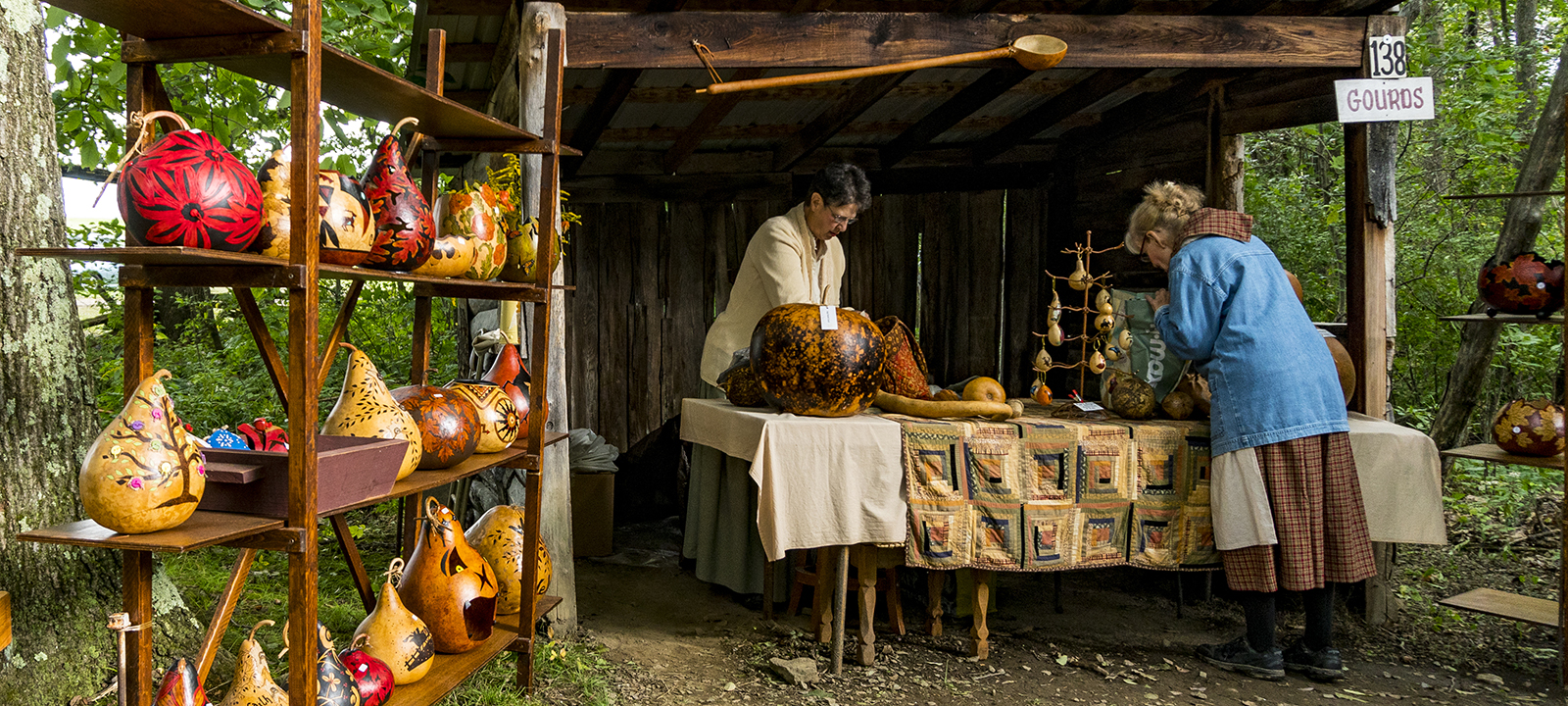 Two women work in a booth filled with decorated gourds for sale.