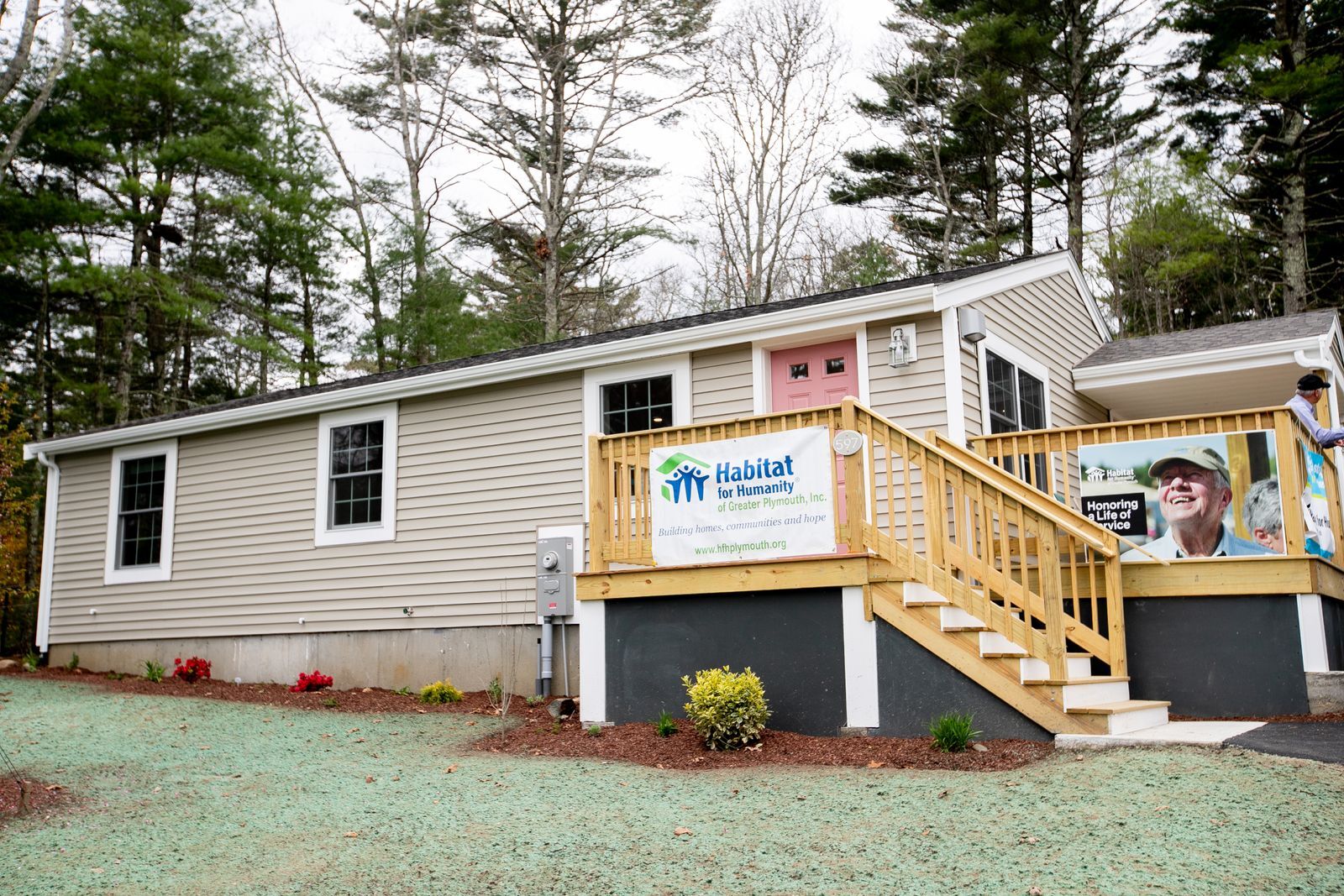 A photo of the exterior of the completed home with beige siding and a taupe door. There  is a Habitat for Humanity of Greater Plymouth sign on the front porch