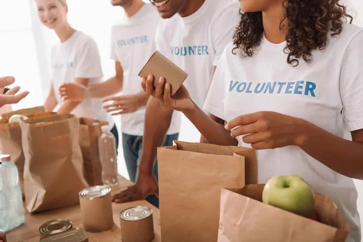 Volunteers packing food items into brown paper bags at a table.