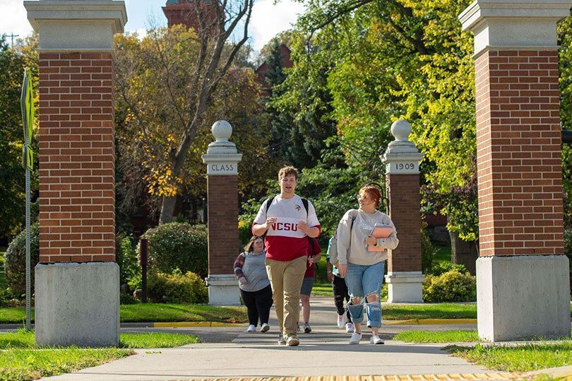 Students walking along the main sidewalk in front of VCSU's campus after class, engaged in conversation, while carrying books and backpacks