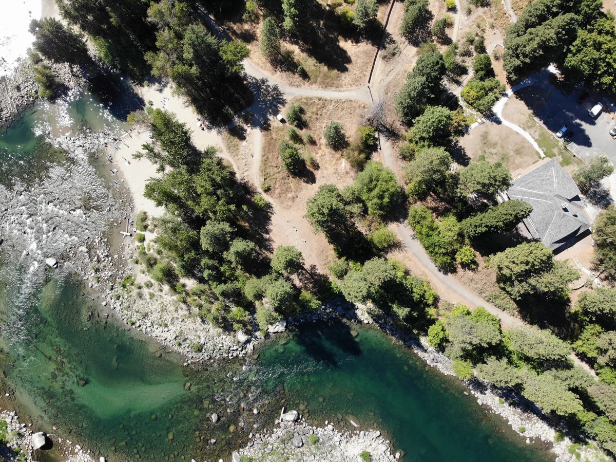 A bird's eye view of the WRI Campus via drone, featuring a building, parking lot, trails, and the Wenatchee River.