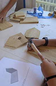 Student hammering a nail into a wooden birdhouse piece