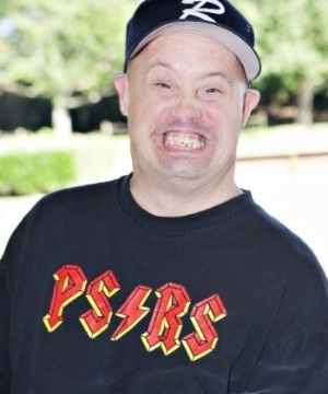 Man with Downs Syndrome supported by PSRS wearing a blue baseball cap and a PSRS Tshirt, looking at the camera with a big smile.
