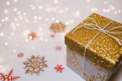 A gift wrapped in glittering snowflake paper surrounded by paper snowflakes and twinkle lights.
