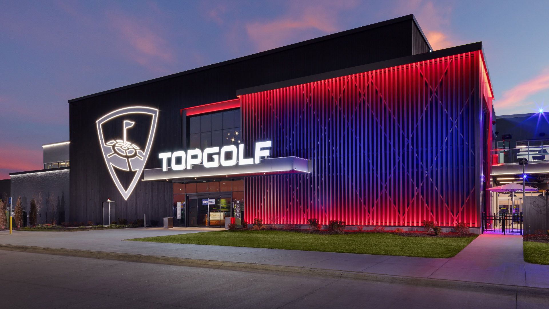 Top Golf building lit up at night with a sunset in the background