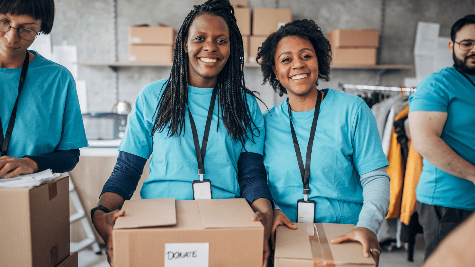 Two women holding boxes smiling looking straight ahead. 