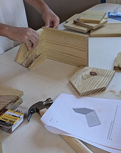 Birdhouse walls being assembled on a table with tools and instructions nearby