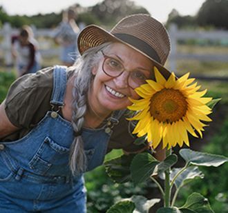Older woman smiles with sunflower outside in a garden