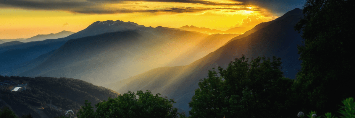 sun shining brightly over dark green mountains and trees