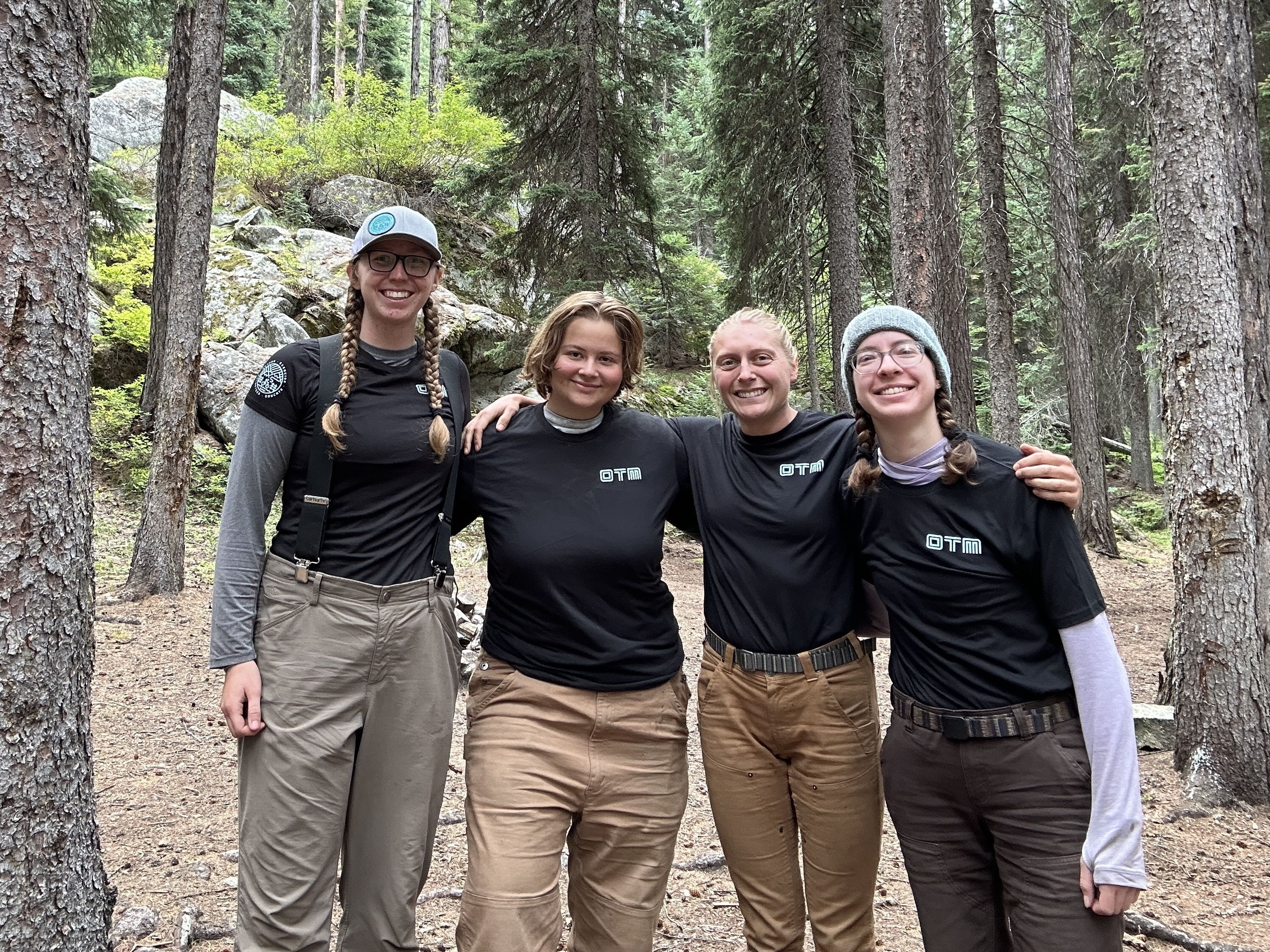 The crew stands smiling, wearing black t-shirts with the "OTM" logo in white.