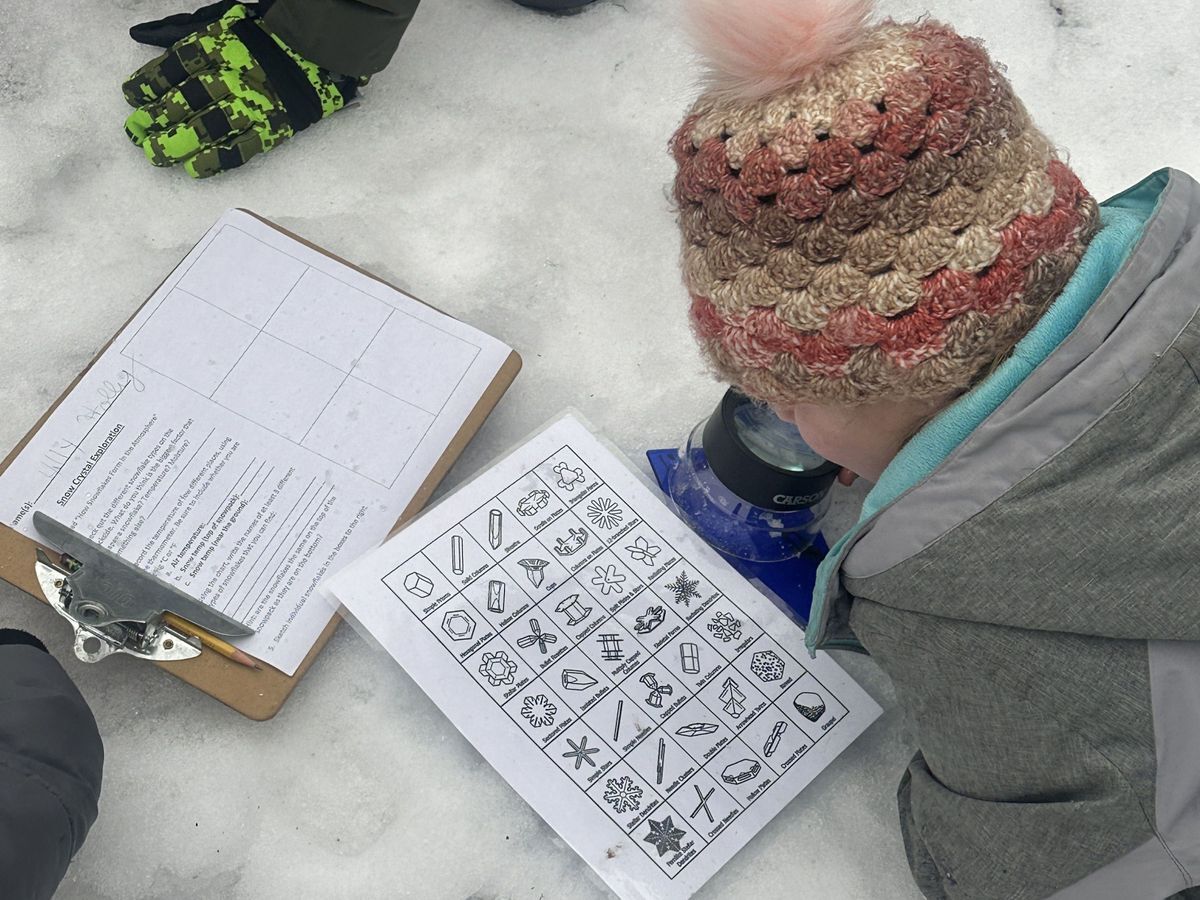 One student dressed in winter gear studying snow crystals with their guide in the snow.