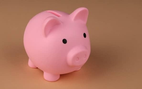 Photo of a pink piggy bank with black eyes set on a copper, metallic background.
