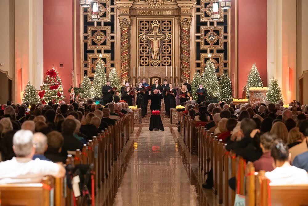 Incoming Artistic Director James K. Bass leads 13 Seraphic Fire singers performing on a church alter in front of festive holiday decorations.