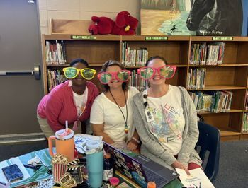 three women in a school library wearing very large playful sunglasses