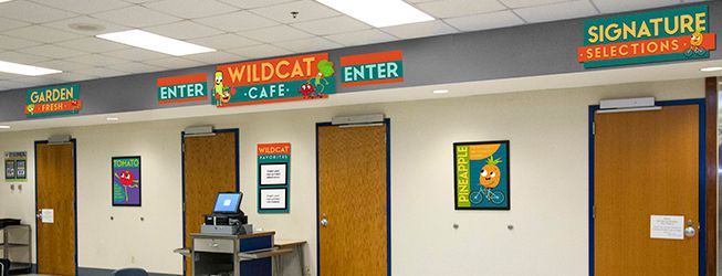 Cafeteria signs above entrance doors, orange and blue with fruits and vegetable nutrition characters