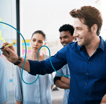 Man drawing on a glass board with colleagues watching.