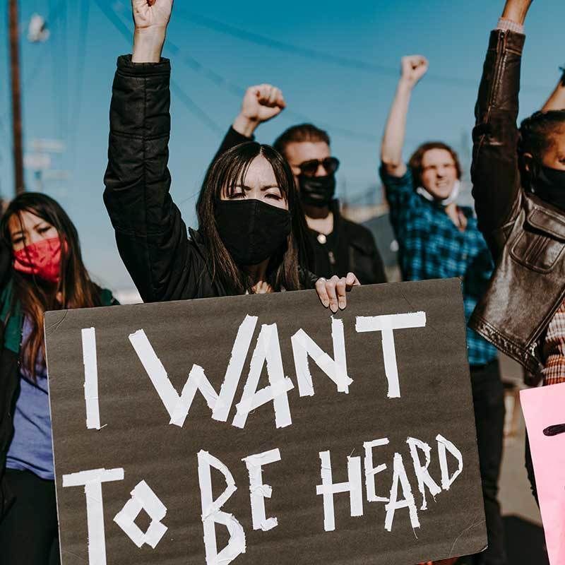A group of people with fists raised holding a sign that reads: I want to be heard.