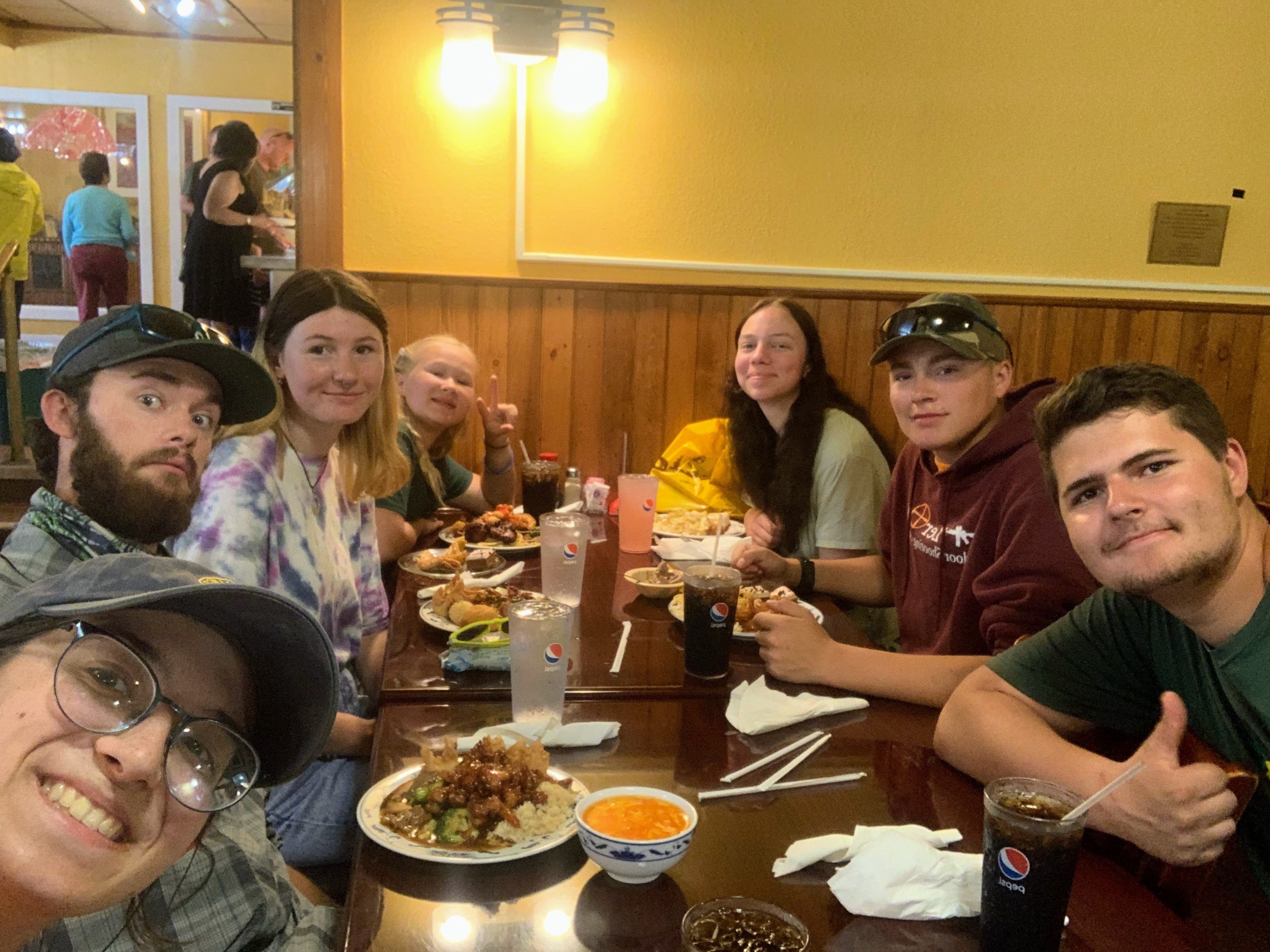 A group of teens and adults sits around a table at the Chinatown Buffet in Cody, WY. They are all smiling.
