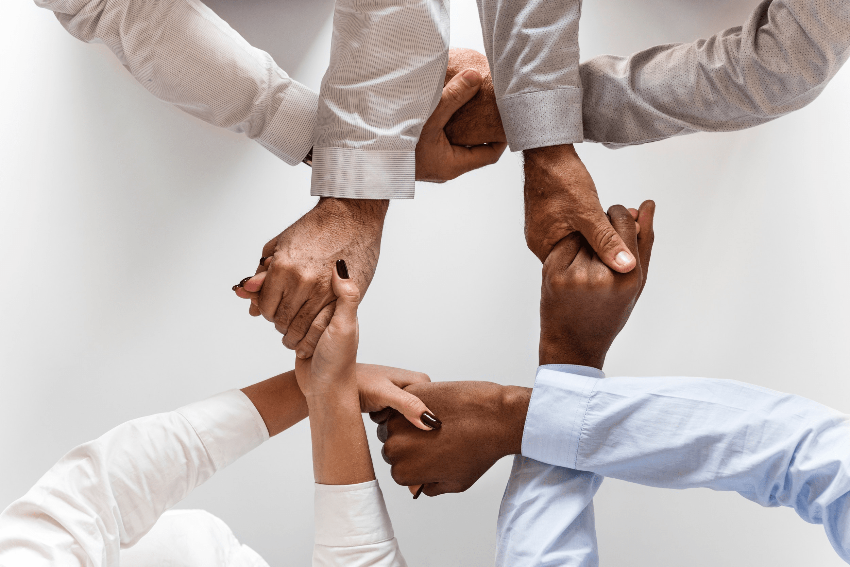 image of four people's hands, men and women with different colors of skin, wearing business shirts, grasping each other in a symmetrical manner, seen from above