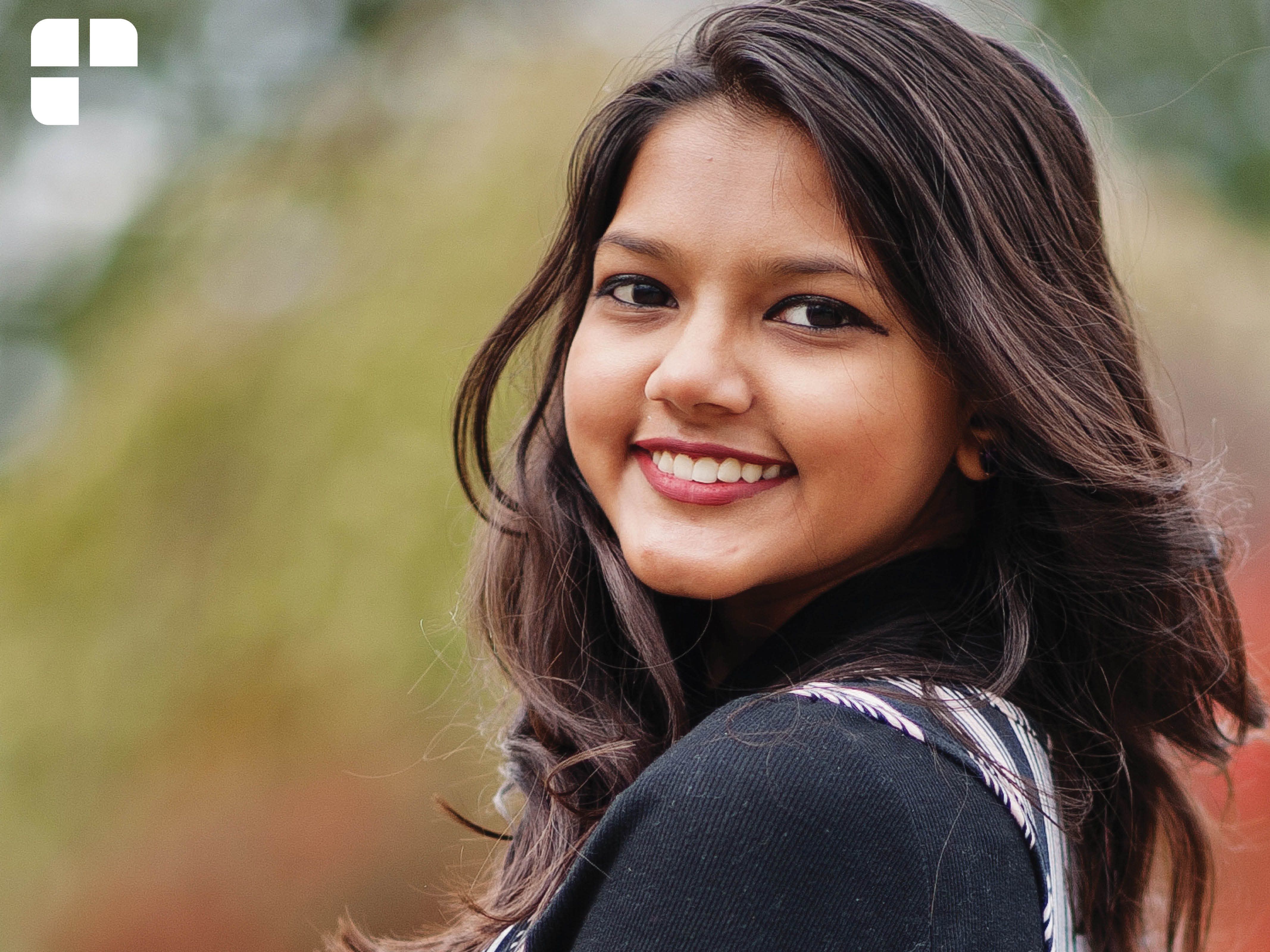 Girl with dark brown hair turning back to look at the camera while smiling.