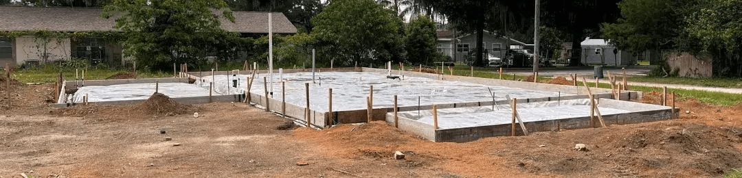 Freshly poured concrete slab foundation for a new Habitat for Humanity home, framed with wooden forms and surrounded by construction stakes