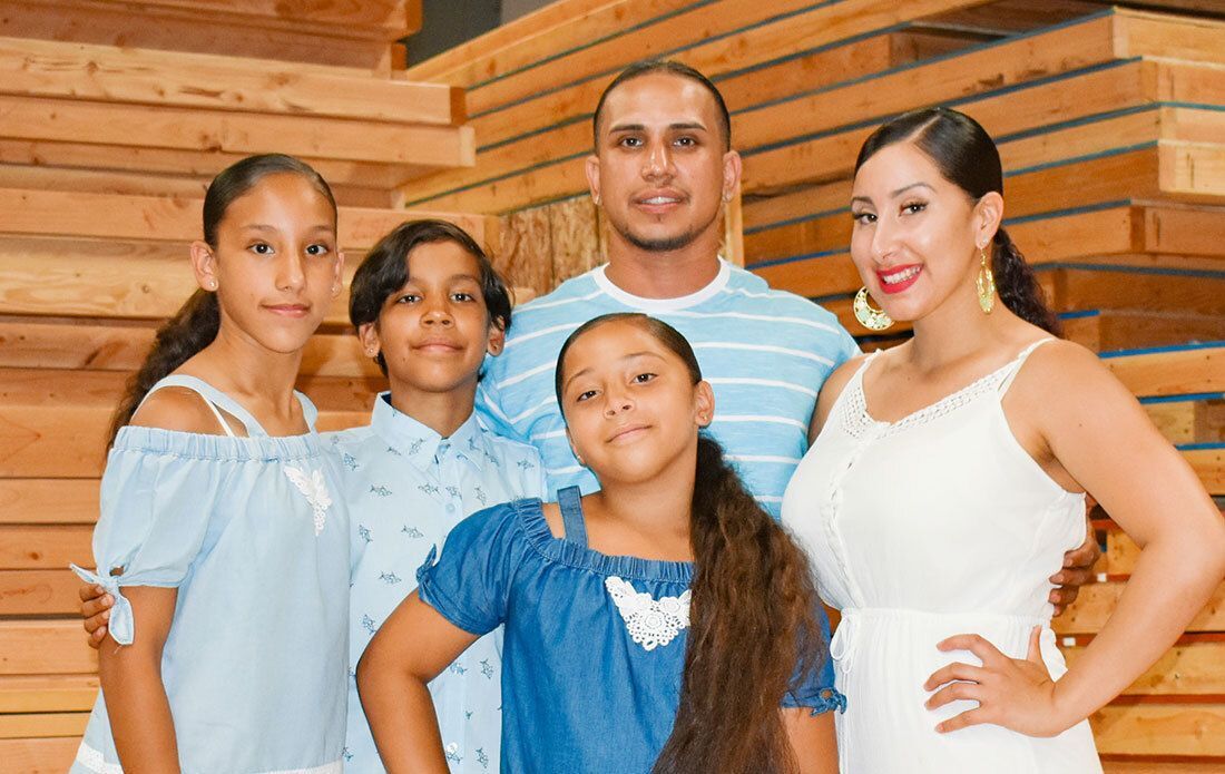 A family of five standing in front of stacked wooden boards.