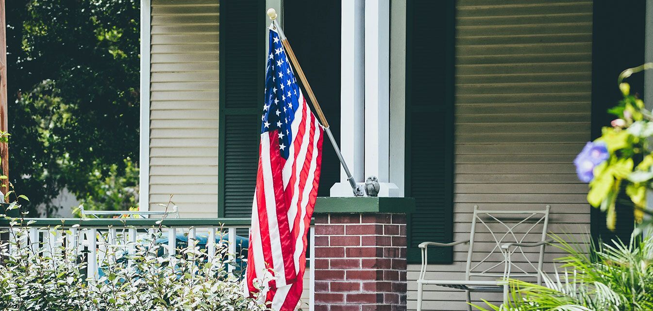 A family in a park, with a woman holding a boy and a man in military uniform saluting a girl.
