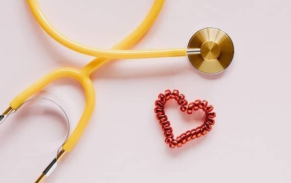 Aerial view photo of a yellow stethoscope and a red heart outline on a light pink background. 