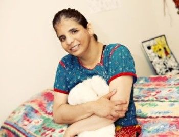Woman supported by PSRS sitting on the edge of her bed, hugging a stuffed animal near her chest and smiling